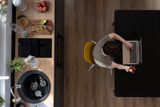 Vista superior mujer joven con laptop en la cocina