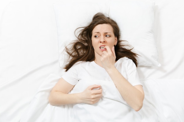 Vista superior de la mujer joven llorando estresada cansada acostada en la cama con sábana blanca, almohada, manta. Pensativo frustrado triste mujer molesta pasar tiempo en la habitación