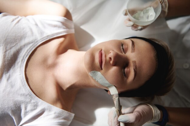 Foto vista superior de la mujer joven que recibe tratamientos de belleza de spa y esteticista aplicando máscara de alginato en su rostro. concepto de cuidado de la piel profesional de spa