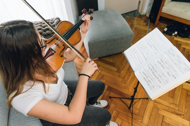 Vista superior mujer joven sentada en casa practicando violín leyendo partituras