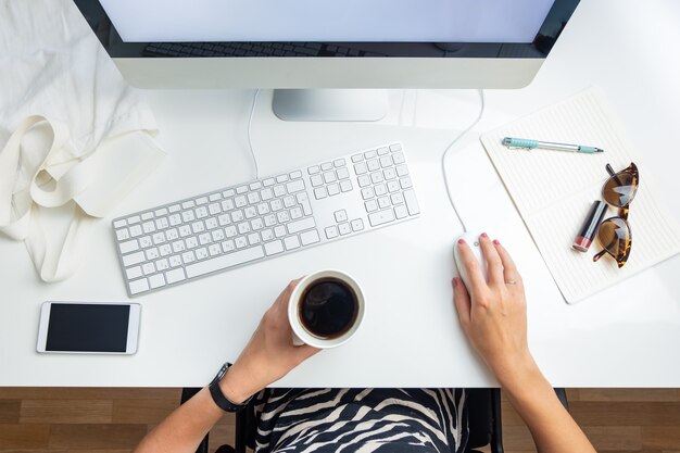 Vista superior de la mujer de negocios en la oficina minimalista. Concepto plano de la vida de oficina: persona femenina con café frente a la computadora de escritorio en el lugar de trabajo