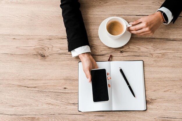 Vista superior de la mujer de negocios que sostiene el teléfono inteligente con pantalla en blanco y taza con café cerca del portátil