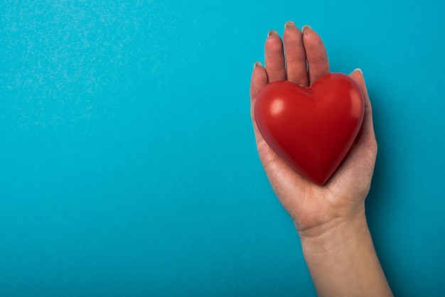 Vista superior de la mujer que sostiene el corazón rojo decorativo sobre el concepto del día mundial de la salud de fondo azul