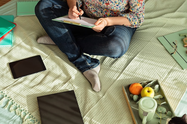 Vista superior de la mujer que trabaja en el entorno informal con su computadora portátil, bloc de notas, taza de té. Trabajo remoto, oficina en casa, autónomo, concepto de autoaislamiento