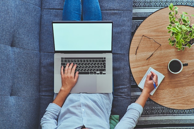 Vista superior de la mujer que trabaja en línea en la computadora portátil y escribir notas en el cuaderno.