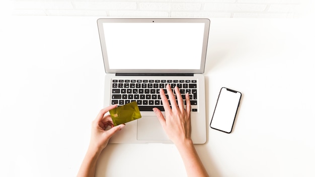 Foto vista superior de la mujer que usa la tarjeta de crédito para compras en línea cerca de teléfono celular en la mesa