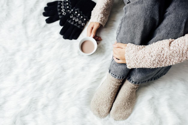 Vista superior de la mujer en ropa de invierno y calcetines sosteniendo una bebida de chocolate caliente