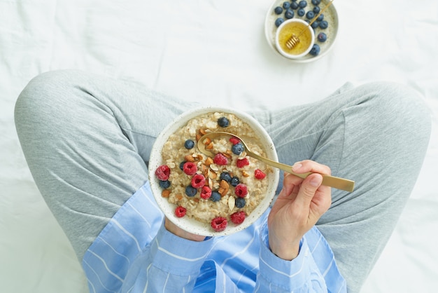 Vista superior mujer sin rostro con plato de avena, sentado en la cama temprano en la mañana