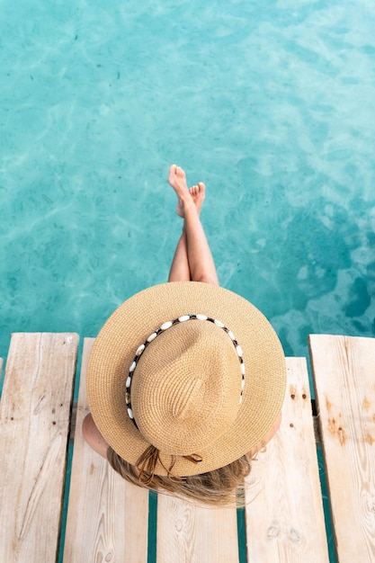 Vista superior de mujer rubia irreconocible con sombrero sentado frente al mar