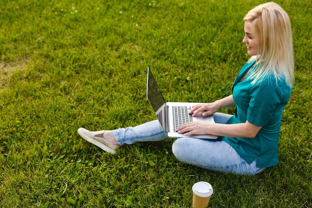 Vista superior de una mujer sentada en el parque sobre la hierba verde con una laptop, con las manos en el teclado. Maqueta de pantalla de computadora. Estudiante estudiando al aire libre. Copiar espacio para texto