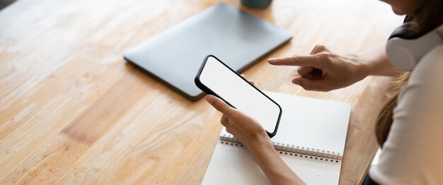 Vista superior Mujer sentada y sosteniendo pantalla en blanco simulacro de teléfono móvil en escritorio de madera