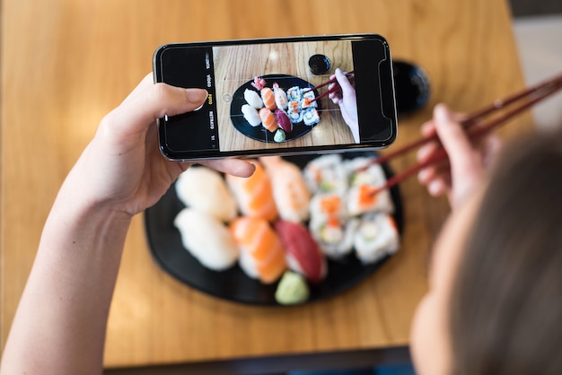 Vista superior de la mujer tomando fotos de sushi en la mesa