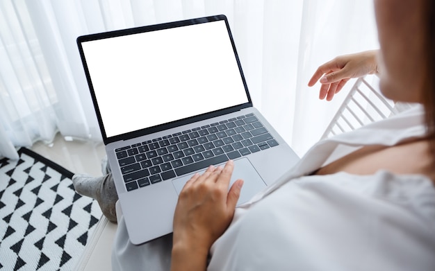 Vista superior de una mujer trabajando y escribiendo en la computadora portátil con pantalla en blanco mientras está sentado en una habitación en casa