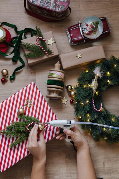 Vista superior de una mujer usando una pistola de pegamento para pegar juguetes a una corona de Navidad estado de ánimo de vacaciones