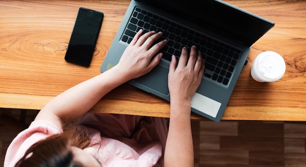 Vista superior de una mujer usando su computadora portátil en el mostrador de madera en un café