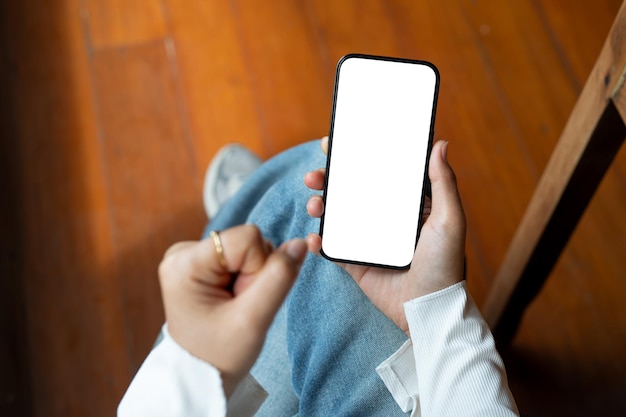 Vista superior de una mujer usando su teléfono inteligente mientras está sentada en el interior Una maqueta de teléfono inteligente con pantalla blanca