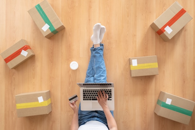 Vista superior de las mujeres que trabajan con la computadora portátil desde casa en un piso de madera con paquete postal, concepto de venta de ideas en línea