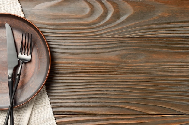 Foto vista superior na faca de prato de barro vazio e garfo de lado no guardanapo cinza na mesa da cozinha de madeira marrom
