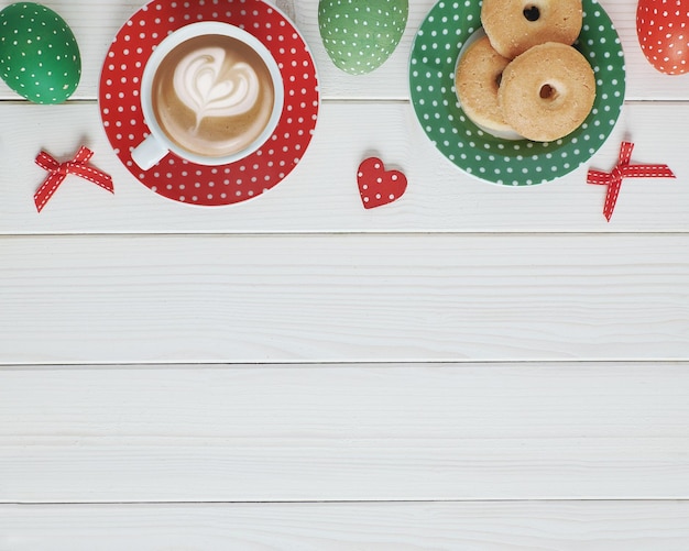 Vista superior na mesa de madeira branca com prato de xícara de café expresso de biscoitos ovos de páscoa em design de bolinhas vermelhas e verdes espaço de conceito de café de primavera para copyspace de texto