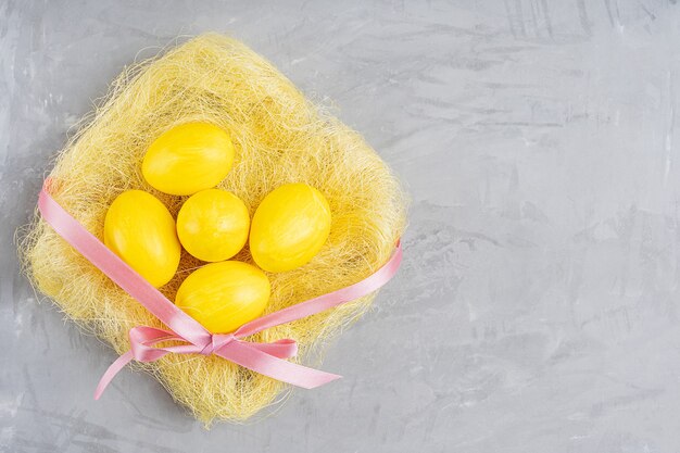 Vista superior del nido de heno con huevos de pascua teñidos en color amarillo om hormigón gris