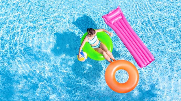 Vista superior de la niña en un anillo inflable verde junto a un rosa y uno naranja en una piscina