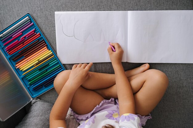 Vista superior de una niña dibujando en un álbum con lápices de colores