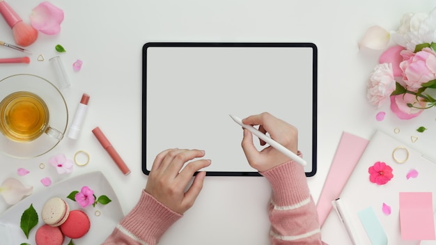 Vista superior de la niña escribiendo en la tableta de la pantalla en blanco en el espacio de trabajo femenino rosa dulce