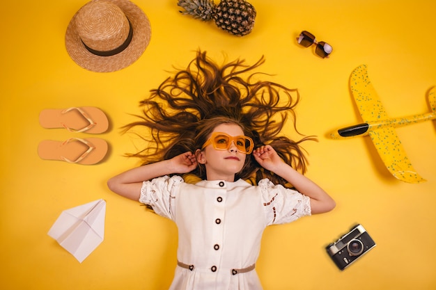 Vista superior de una niña con gafas amarillas que viaja, colección de artículos de ocio sobre un fondo amarillo