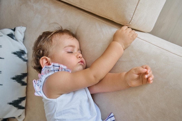 Vista superior de una niña pequeña acostada en un cómodo sofá y durmiendo una siesta en la sala de estar en casa