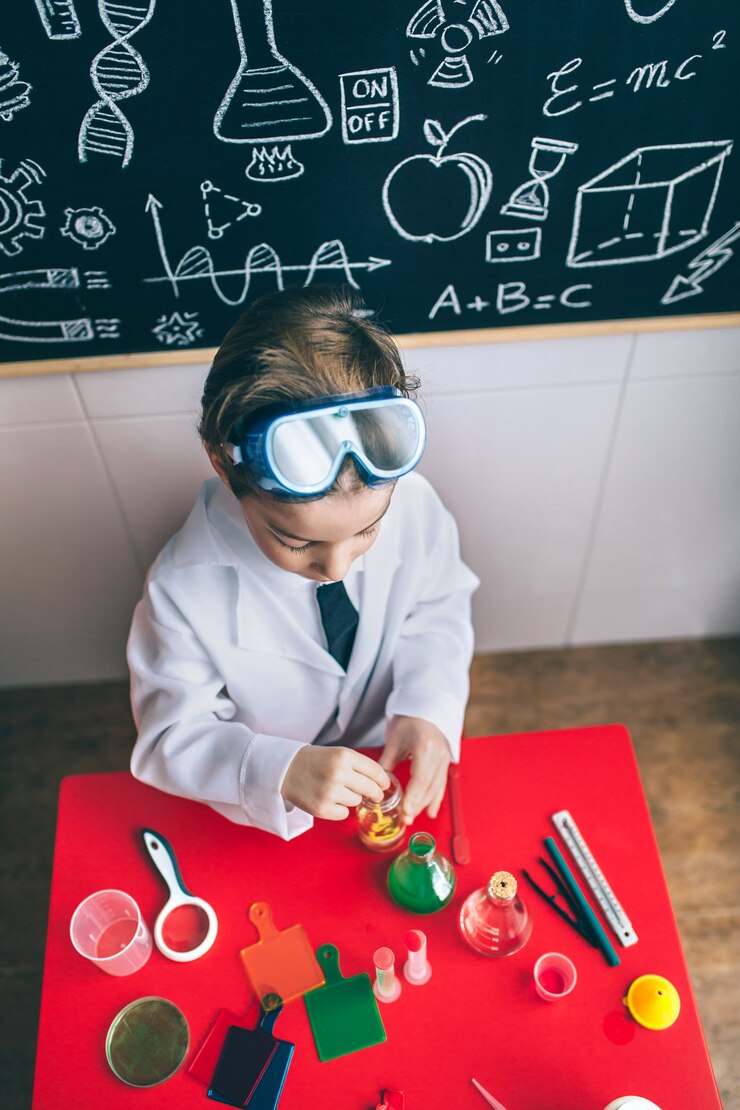 Foto vista superior del niño científico jugando con líquidos químicos sobre la mesa contra la pizarra con dibujos