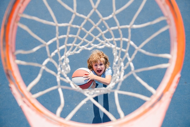 Vista superior del niño emocionado jugando baloncesto sosteniendo la pelota con cara feliz.