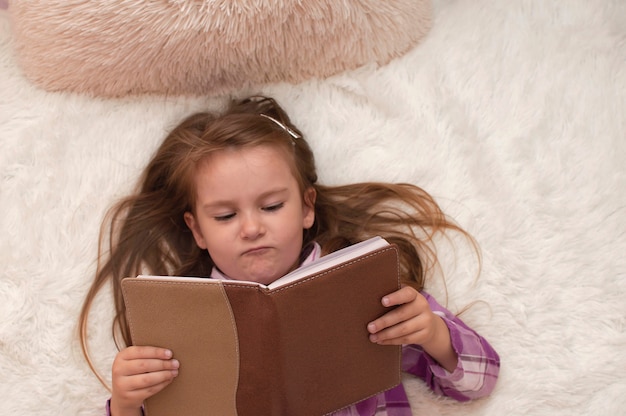 Vista superior. El niño está acostado en la cama y estudia un libro. Una niña está leyendo un libro en una cama en una habitación luminosa. Enfoque selectivo.