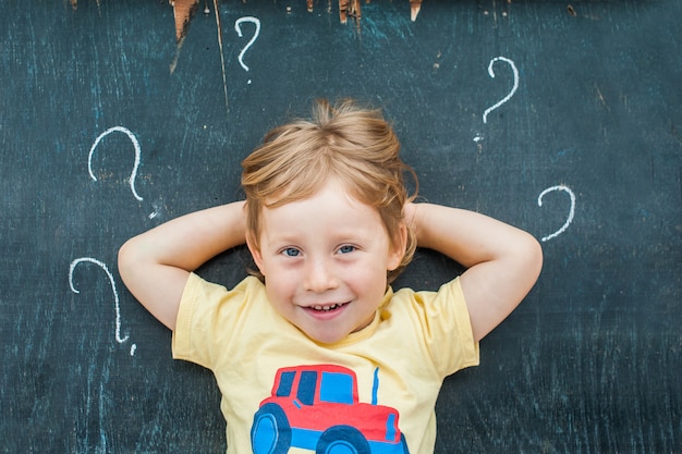 Vista superior de un niño pequeño niño rubio con signo de interrogación en la pizarra