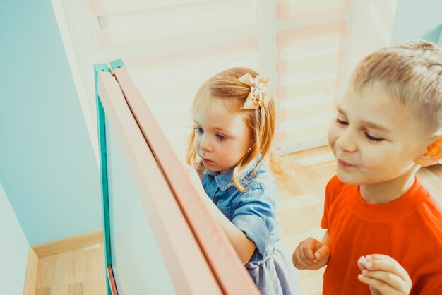 Vista superior de un niño sonriente y una niña linda dibujando en una pizarra en el jardín de infantes