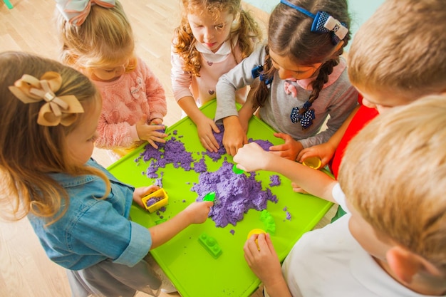 Vista superior de niños pequeños haciendo formas con arena cinética en la mesa de juego