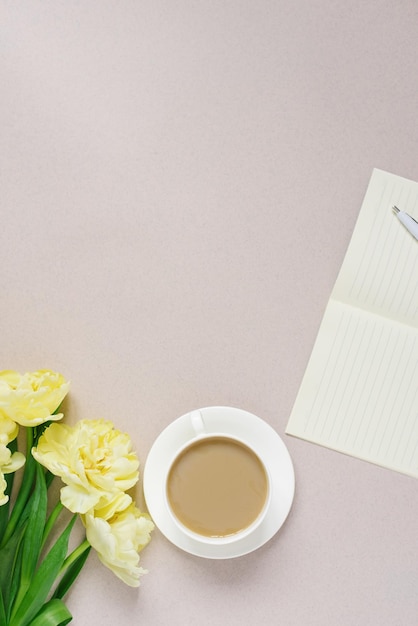 Vista superior no fundo de uma área de trabalho com um bloco de notas e uma caneta com uma xícara de café com leite plana flores de tulipa amarela plana Área de trabalho lcopy espaço de trabalho artigos de papelaria