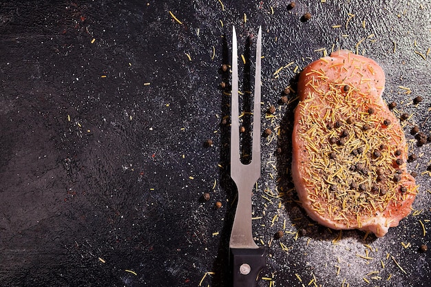 Vista superior no pedaço de carne de bife cru temperado com pimenta, sal e alecrim seco na mesa de madeira escura