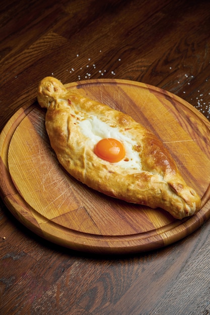 Vista superior no saboroso Adjarian Khachapuri tradicional - abra a torta assada com queijo derretido sal (suluguni) e gema de ovo na bandeja de madeira. Comida georgiana tradicional