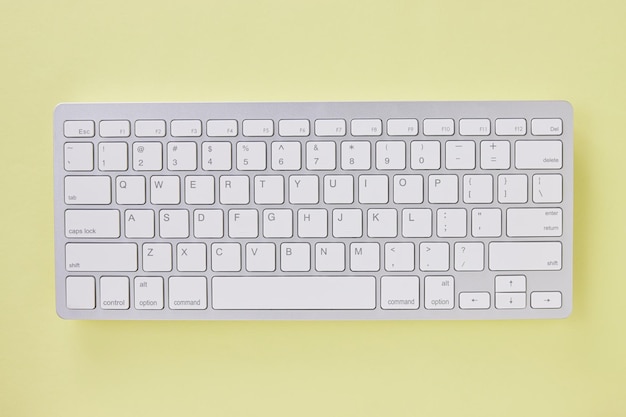 Vista superior o plana teclado de computadora inalámbrica blanco en fondo de mesa de oficina de color amarillo pastel