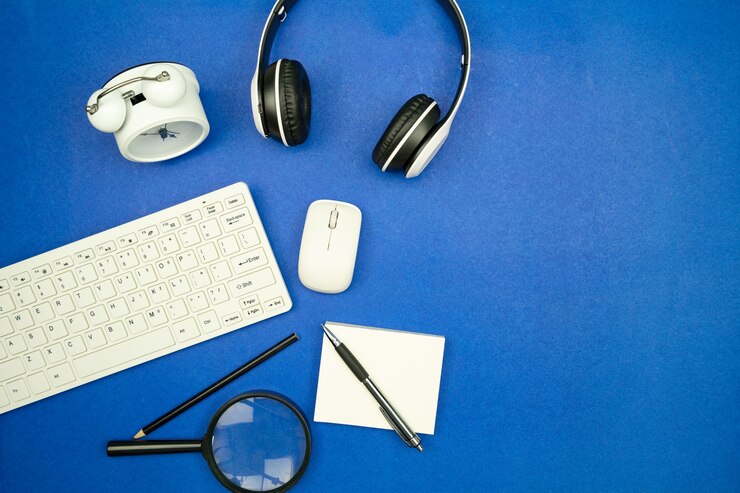 Foto vista superior de los objetos comerciales teclado, mouse, auriculares, papeleo con lápiz y reloj despertador sobre fondo de papel azul