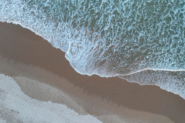 Vista superior de la ola rompiendo en la arena dejándola con diferentes tonos