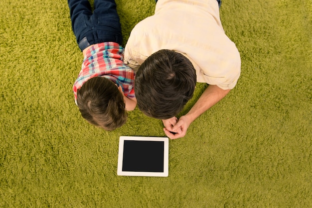 Vista superior del padre mostrando a su hijo cómo usar la tableta