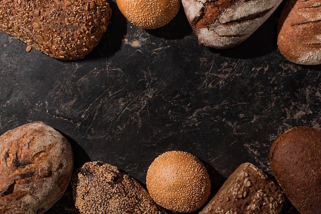 Vista superior de pan y bollos recién horneados en la superficie negra de piedra