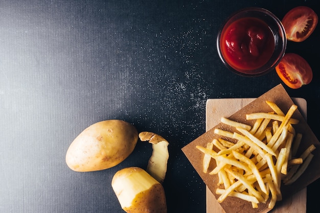 Vista superior de papas fritas con salsa de tomate y patatas crudas en bacground negro. copia espacio