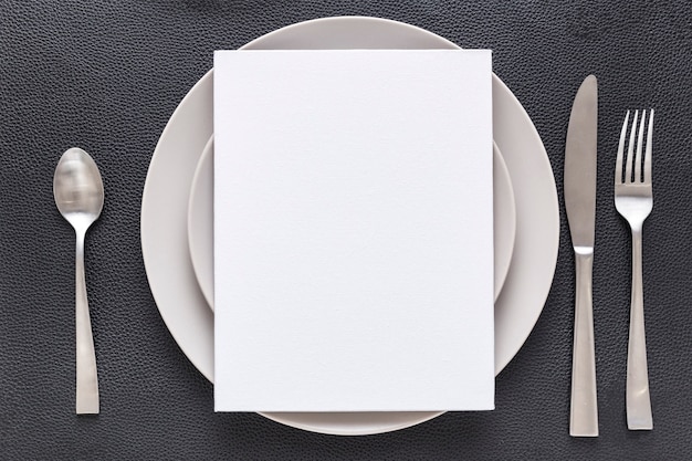 Vista superior del papel de menú en blanco en un plato con tenedor y cuchillo