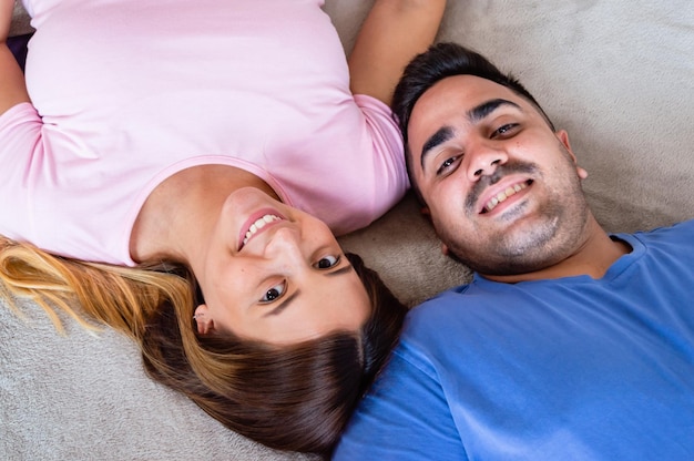 vista superior de una pareja heterosexual juntos acostados en la cama mirando a la cámara y sonriendo