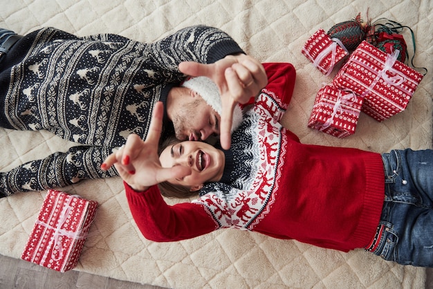 Vista superior de la pareja en ropa de Navidad yace en el suelo con regalos.