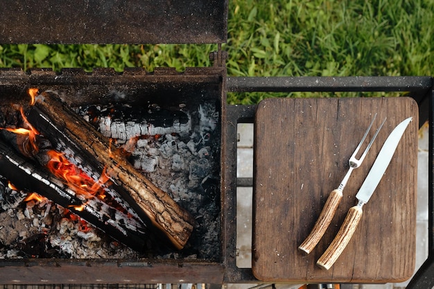 Vista superior de la parrilla de metal con troncos encendidos y tenedor y cuchillo para bistec