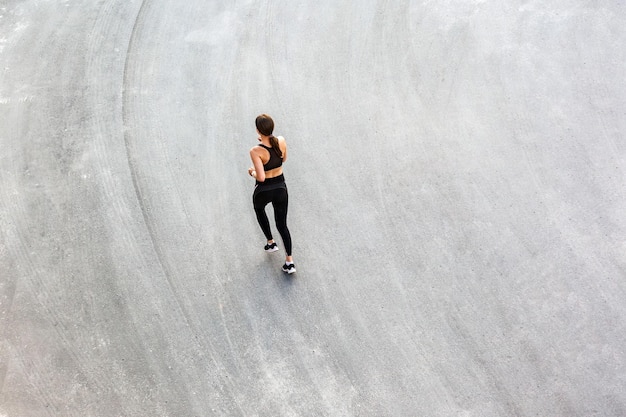 Vista superior de la parte trasera de una joven y atractiva mujer atlética que corre sobre el asfalto de la ciudad y hace ejercicio por la mañana en un día soleado de verano Corredora entrenando al aire libre Concepto de deporte Copyspace