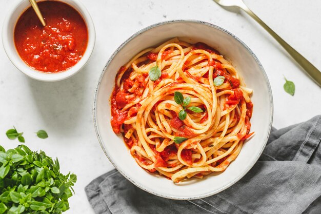 Vista superior de la pasta tradicional con salsa de tomate y albahaca griega en un cuenco de cerámica sobre una mesa blanca